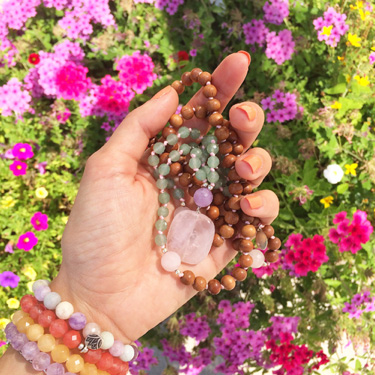 A hand holding beads in front of flowers.